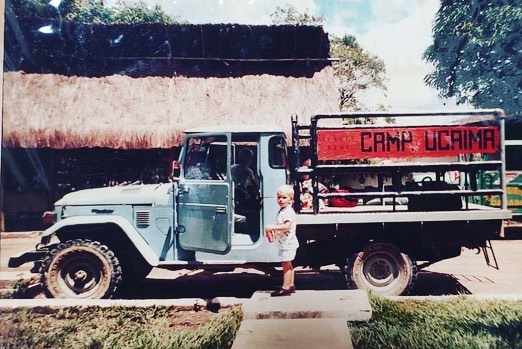 Un camión con el letrero Camp Ucaima frente a una construcción de palma.